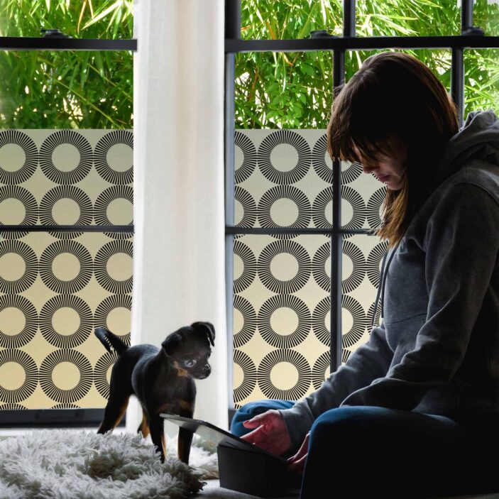 stickpretty_privacy_window_film_orba_bk.jpg A girl and puppy sit by a window covered in Window Privacy Film. THe patter is a bold black circular repeat.
