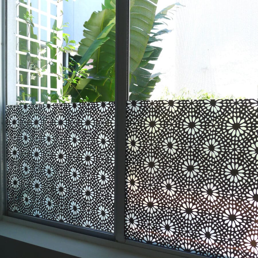 Window privacy film adorns the bottom half of a window. The pattern features an all-over print of small a symmetric petals and flower centers.
