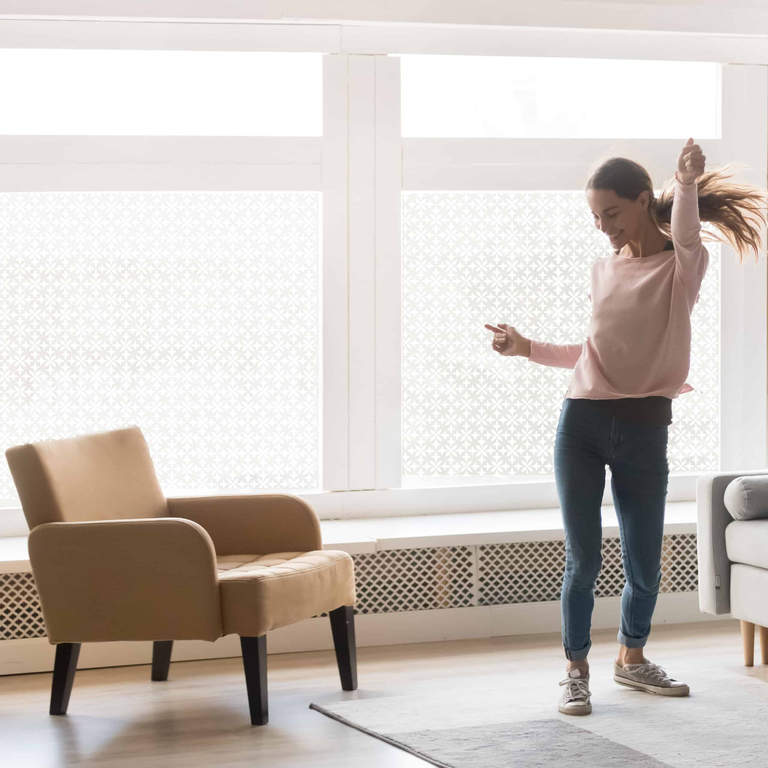 decorative window privacy film covers large living room windows, allowing a woman to dance in private.